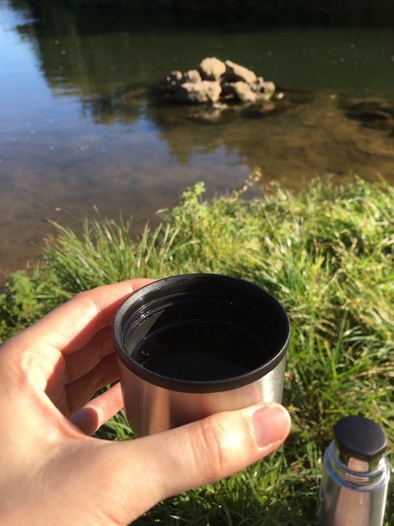 Foto von heißem Tee aus einer Thermoskanne. Im Hintergrund ist ein Fluss zu sehen.